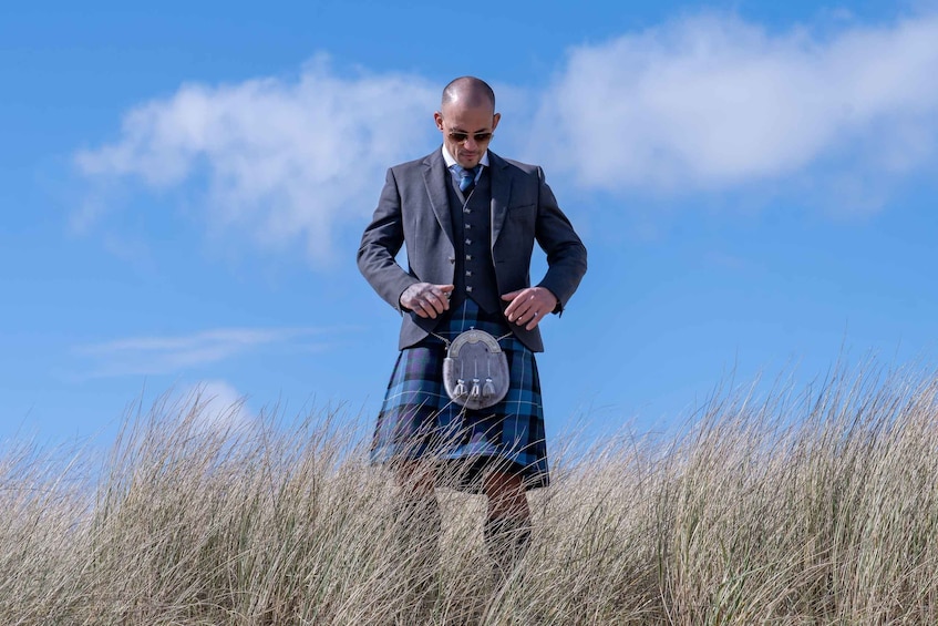A man in a kilt and suit standing in a field. 1