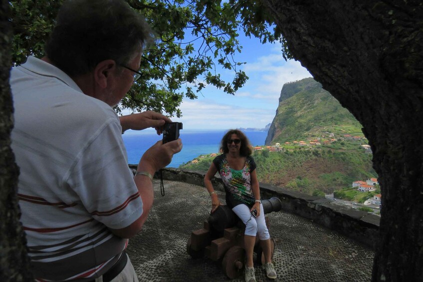 A person taking a photo of another person sitting on a cannon. 3