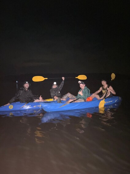 Four people in a blue kayak on a body of water at night. 1