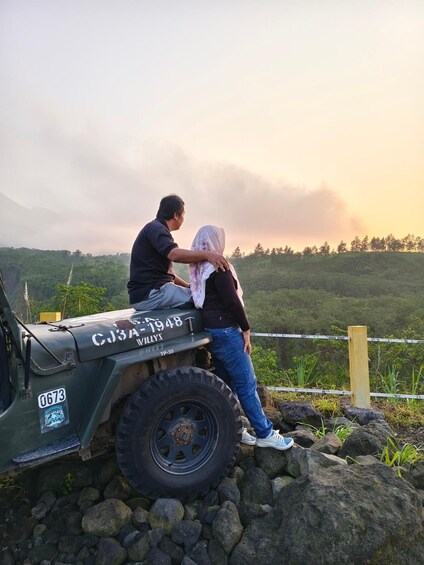 Un hombre y una mujer de pie junto a un vehículo verde con la inscripción 'CJ3A-1948' y 'VILLY', contemplando un paisaje montañoso. 3