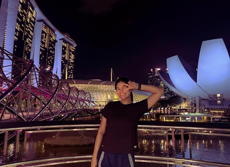 A person standing by a waterfront with modern buildings and a distinctive architectural structure in the background. 5
