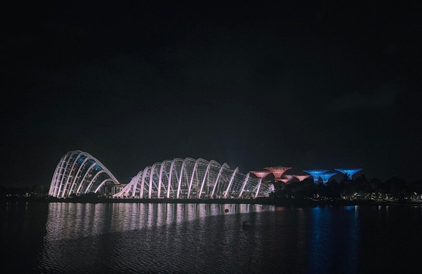 A nighttime view of a large, illuminated bridge with arches reflecting on the water. 1