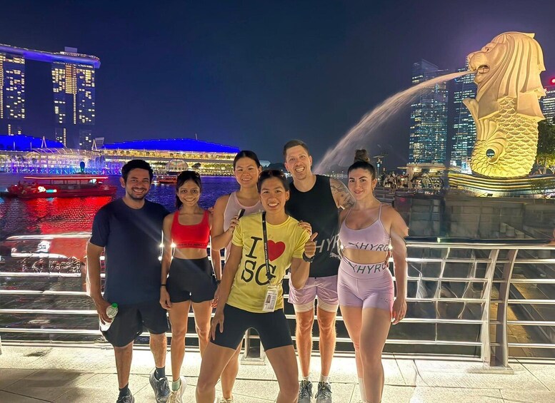 A group of people posing in front of a city skyline with illuminated buildings and a large lion statue. 3