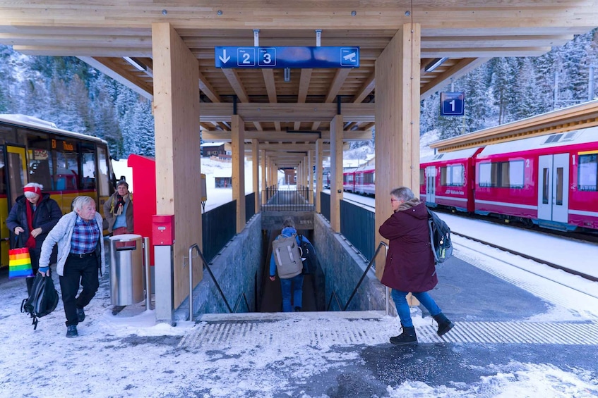 A train station platform with wooden shelters, a red train, and a snow-covered landscape. 3