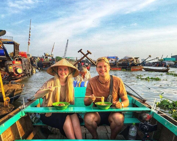 Two people sitting on a boat with green tables, eating bowls of food. 5