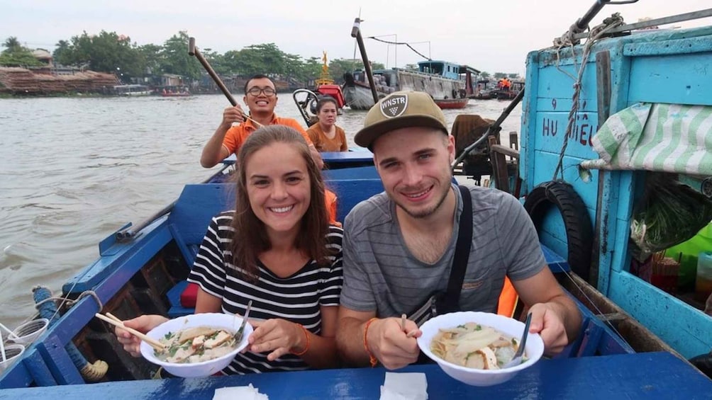 A group of people on a boat, eating bowls of food. 2