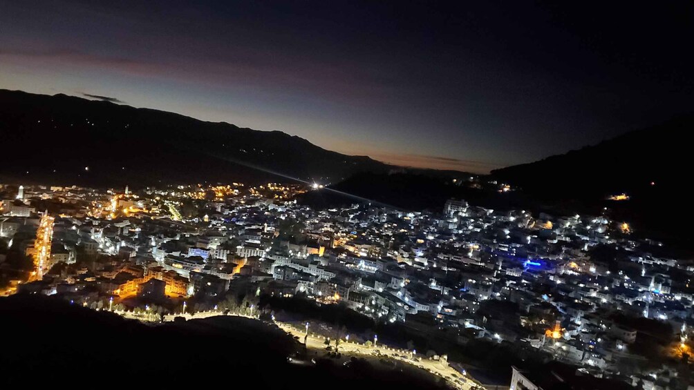 A nighttime view of a densely populated town with illuminated buildings and a mountain backdrop. 2