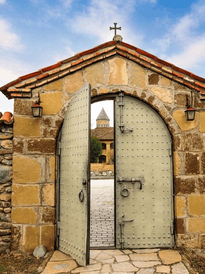 A large, arched metal gate with a cross on top, leading to a stone building with a tiled roof. 2