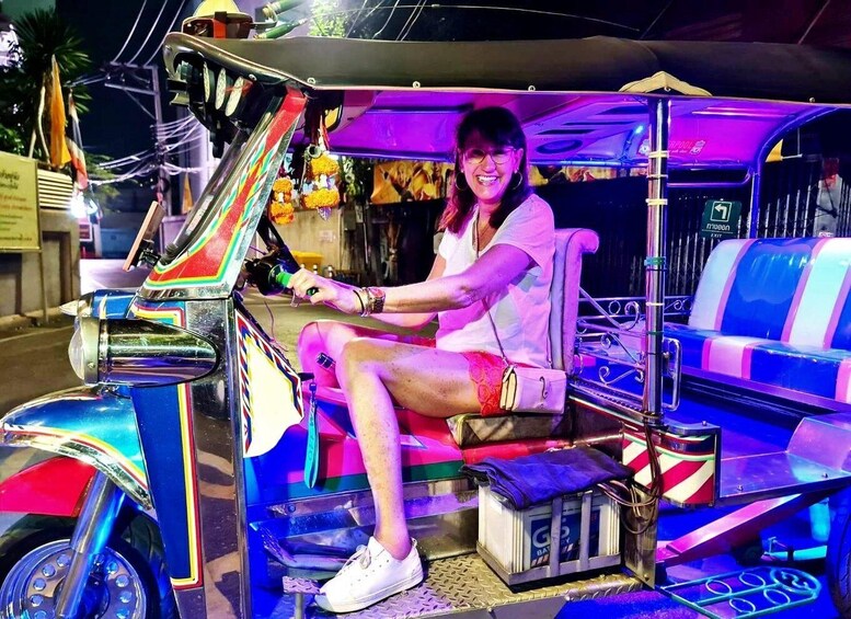 A woman sitting in a colorful tuk-tuk with a battery pack on the floor. 3