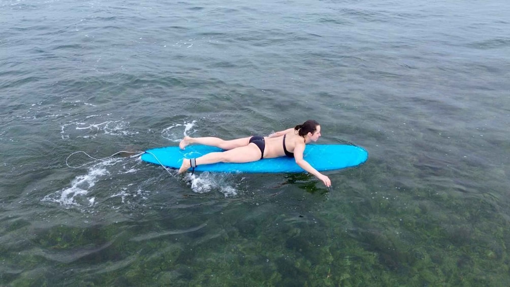 A person lying on a blue surfboard in clear water. 5