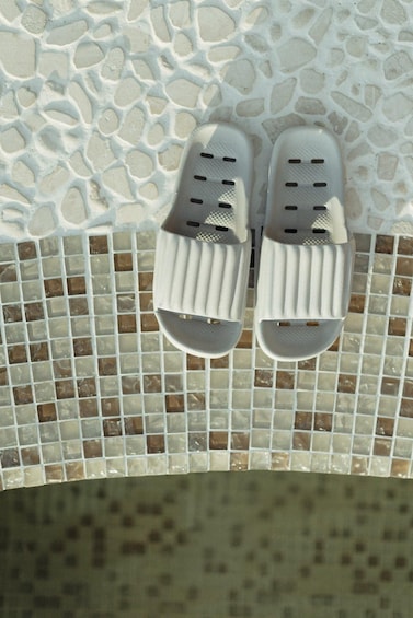 A pair of white sandals with perforations on a tiled surface. 5