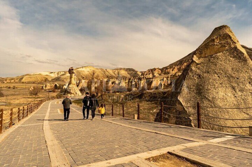 A paved walkway with large rock formations and a fenced area. 1