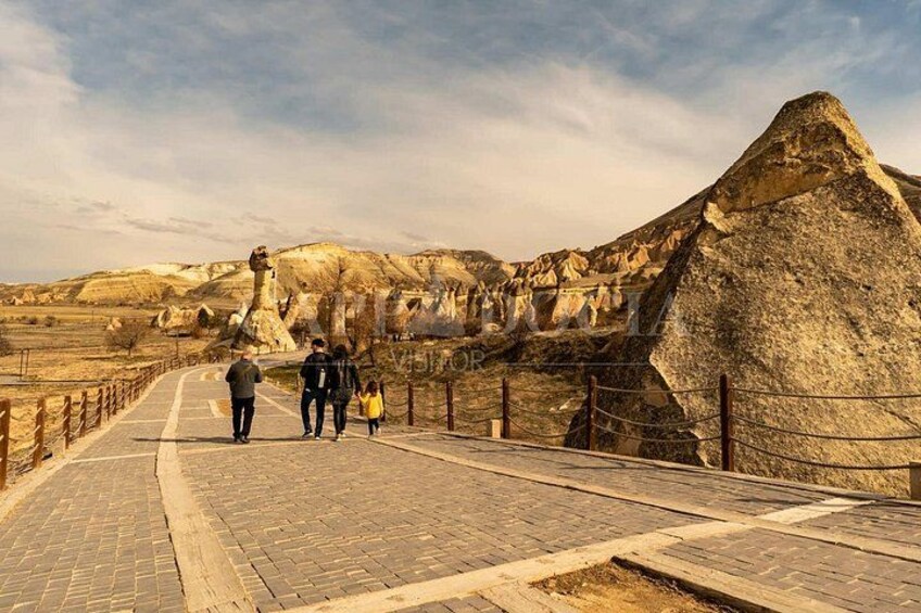 A paved pathway with a fence, rocky terrain, and a large rock formation. 5