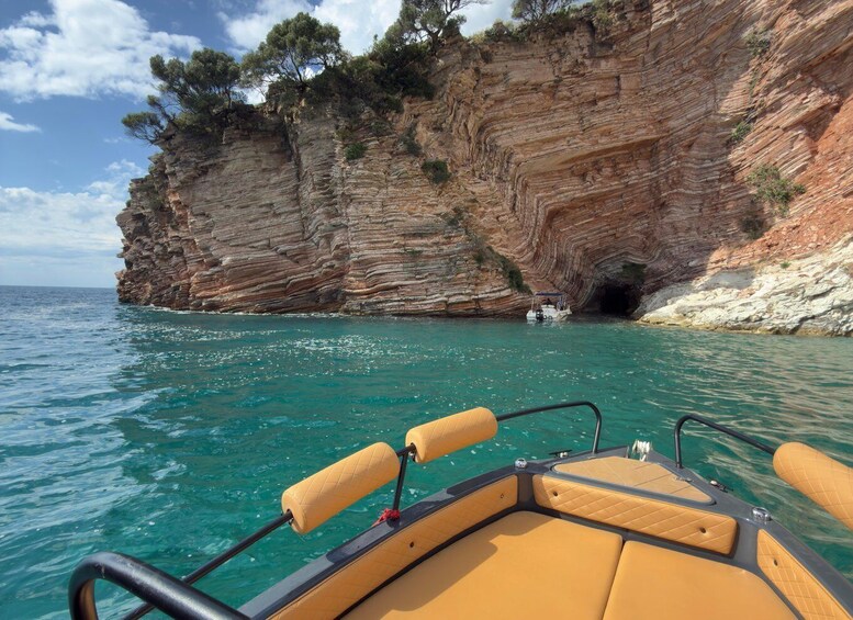 A boat on turquoise sea with rocky cliffs and a cave entrance. 1