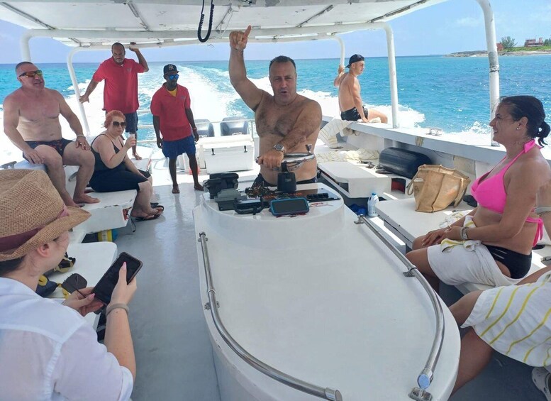 A group of people on a boat with a man standing on the deck, others seated, and a woman in a pink top. 2