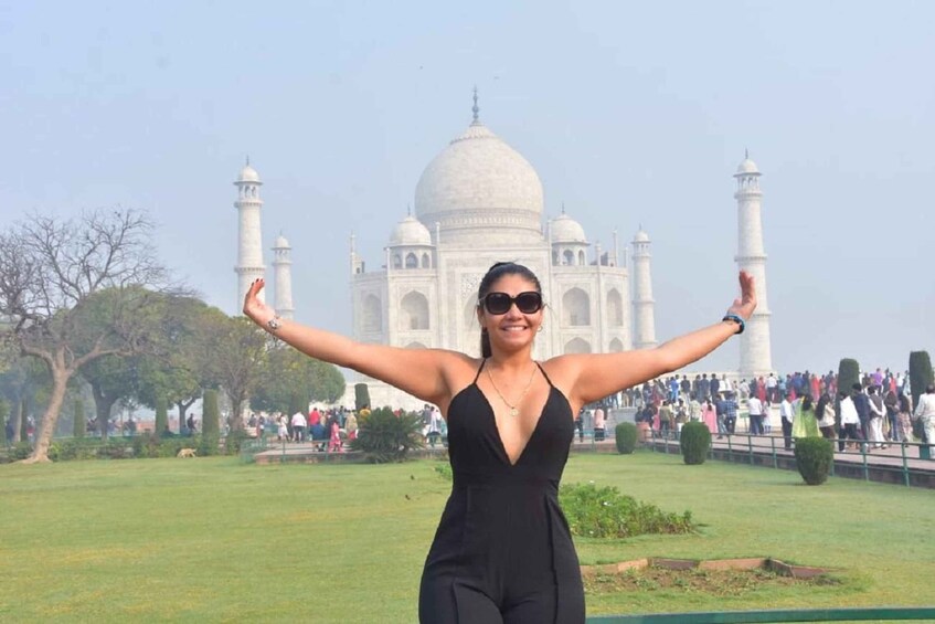 A person in a black outfit with arms outstretched in front of the Taj Mahal. 2