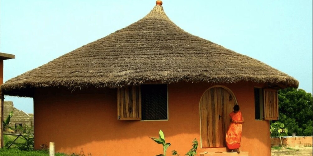A thatched-roof hut with a single door and window, surrounded by greenery. 5