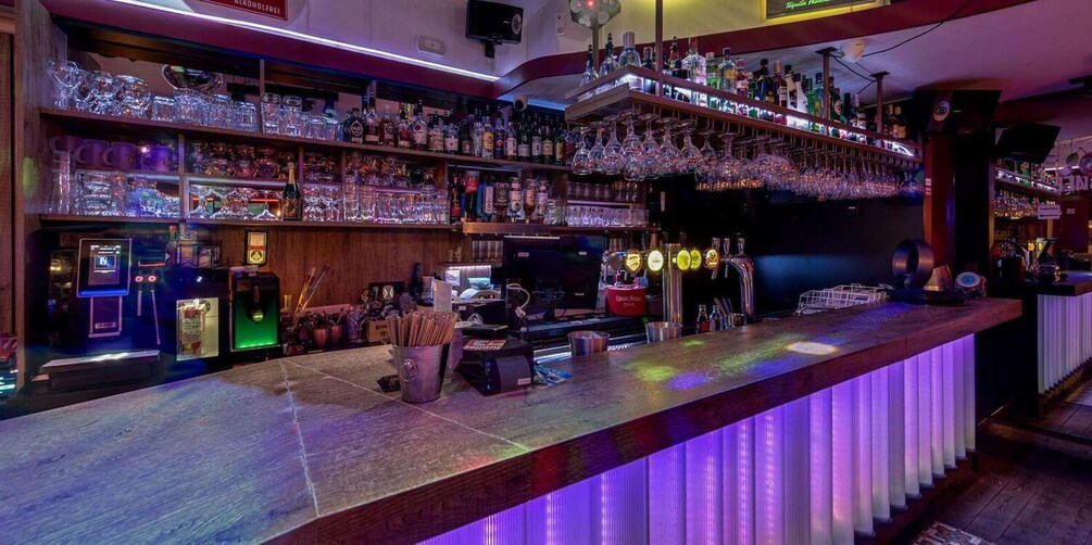 A bar with shelves of bottles and glasses, a cash register, and a neon sign. 3