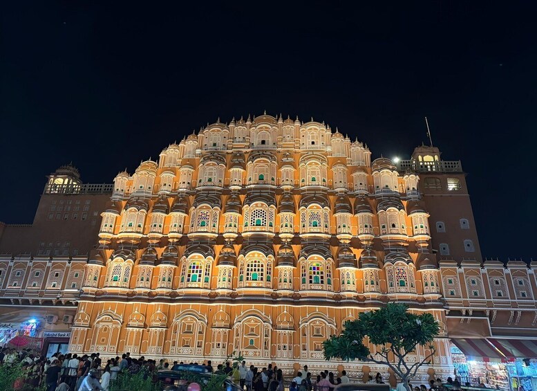 A brightly lit, ornate building with multiple balconies and windows, surrounded by a crowd of people. 3