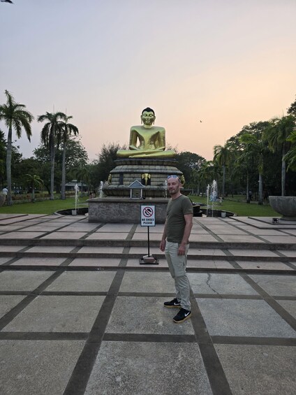 A man standing in front of a large golden Buddha statue with a 'NO SHOES PLEASE' sign. 5