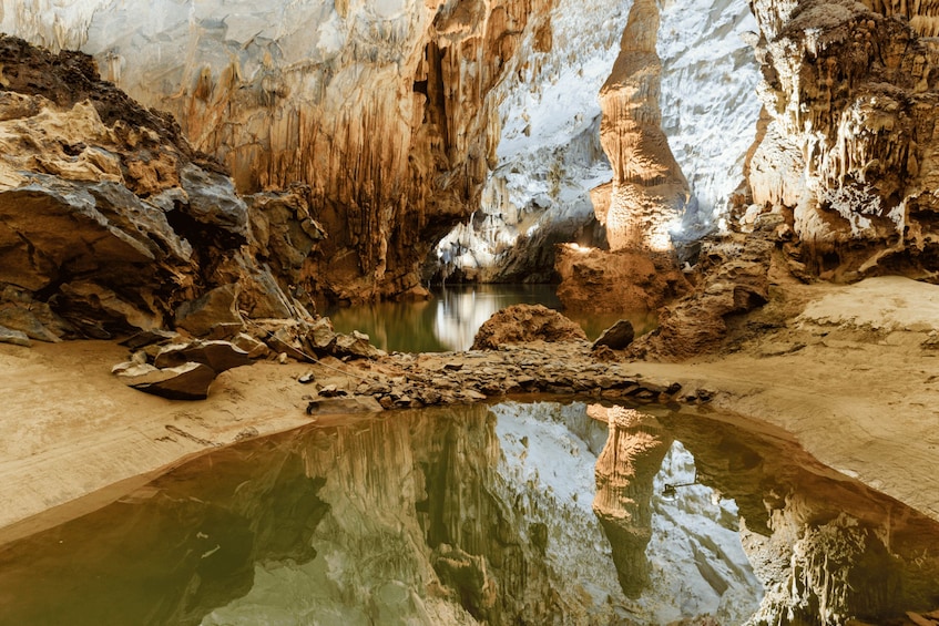 A cave with stalactites, a reflective pool, and a narrow passage. 3
