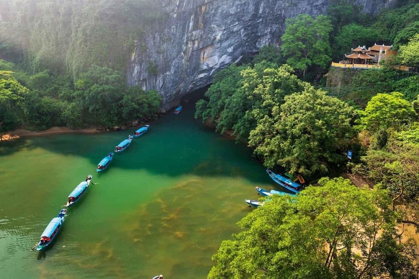 A river with boats, dense greenery, and a building on a cliff. 1