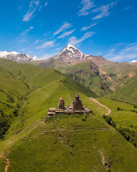 A monastery on a green hillside with a snow-capped mountain in the background. 3
