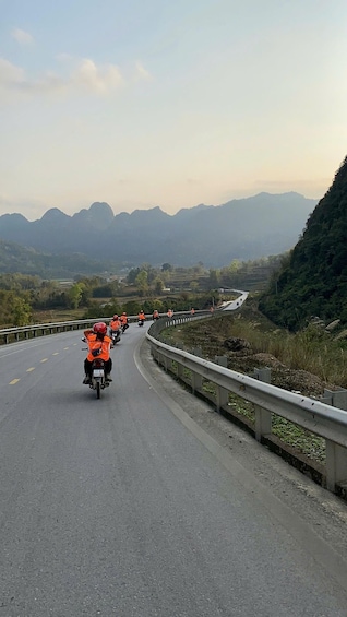 A group of motorcyclists on a winding mountain road with guardrails, surrounded by lush greenery and distant mountains. 1