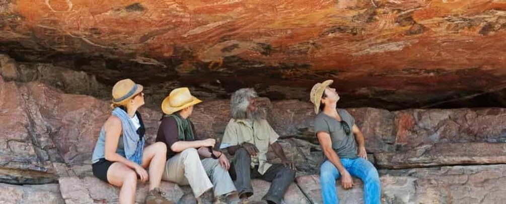 Four people sitting on a rocky ledge under a large rock formation. 1