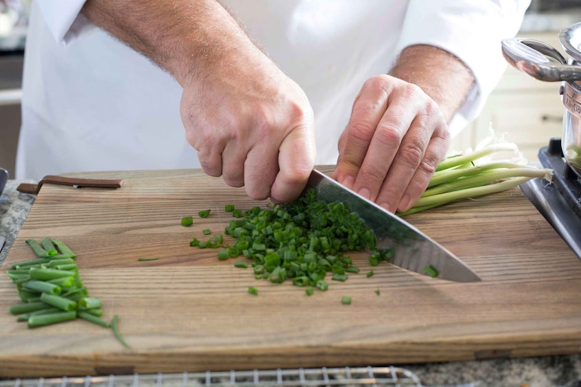 A person chopping green onions on a wooden cutting board. 4