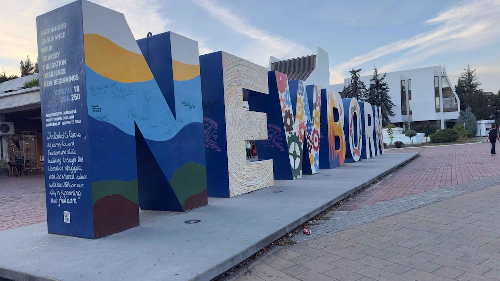 A series of colorful, abstract sculptures with inscriptions and graffiti, located in an urban setting with a paved walkway. 3
