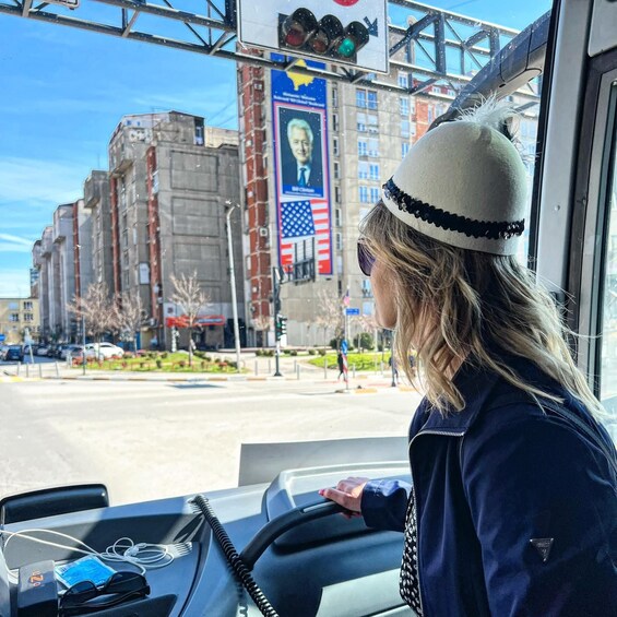 A person driving a bus, with a cityscape in the background including buildings and a traffic light. 2