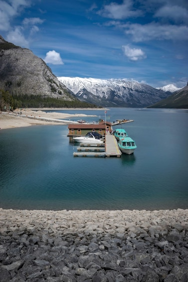 A calm lake with boats docked at a wooden pier, surrounded by mountains and a clear sky. 2