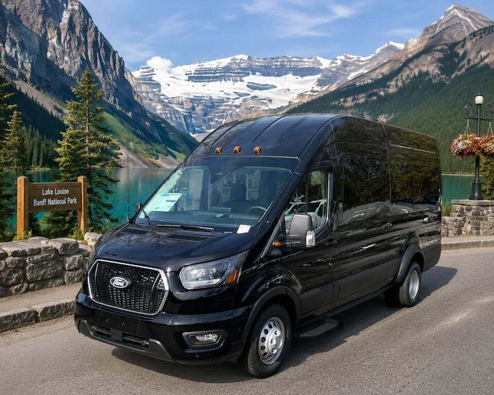 A black Ford Transit van parked on a road with a mountainous backdrop and a sign for Lake Louise Banff National Park. 1