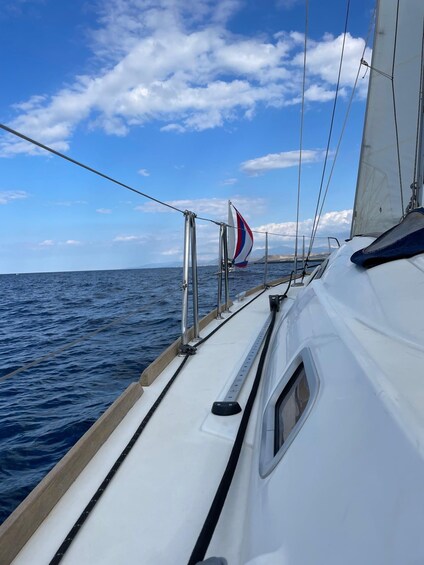 A sailboat with a white hull and a red, white, and blue sail, sailing on a blue sea under a partly cloudy sky. 4