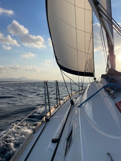 A sailboat with a white hull and a large sail, sailing on open water with a clear sky and distant land visible on the horizon. 5