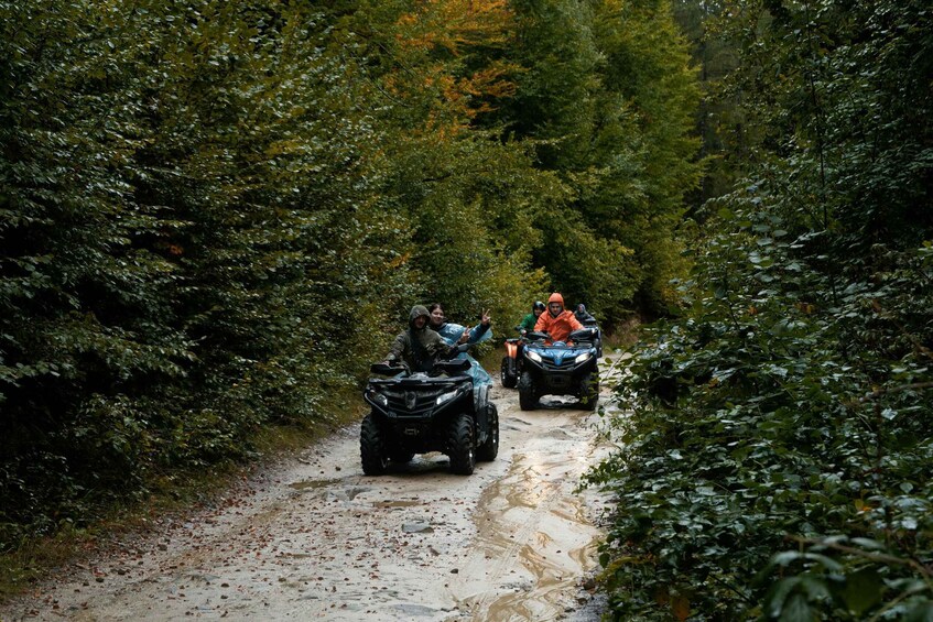 Two people on ATVs on a muddy path surrounded by dense foliage. 2