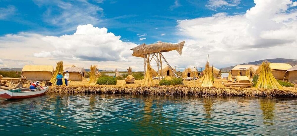 A traditional village by a lake with thatched-roof huts, a wooden fish sculpture, and a boat. 2