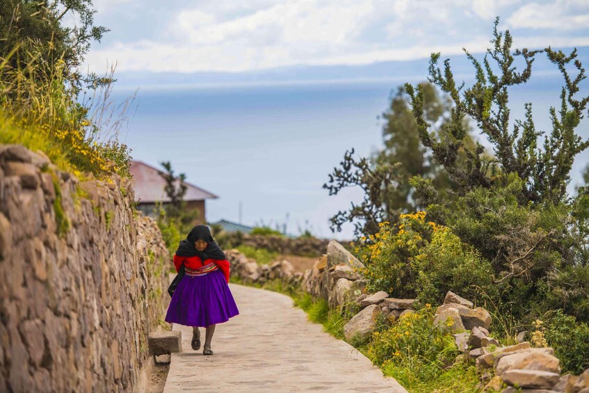 A woman in traditional attire walking on a stone path beside a coastal cliff. 4