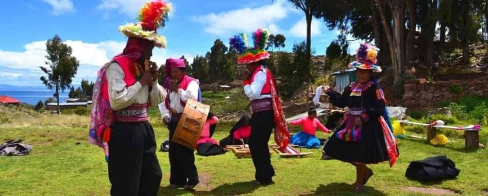 People in traditional attire dancing on a grassy field with trees and a clear sky in the background. 1
