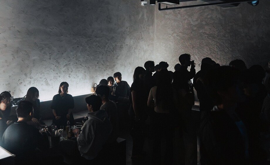 A group of people in a dimly lit room with a textured wall. 3