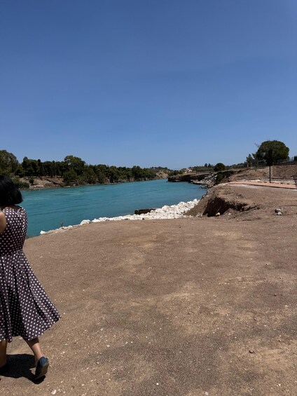 A woman in a polka dot dress walking along a dirt path by a turquoise sea. 4