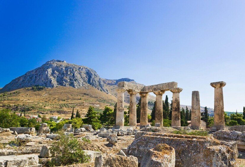 Ancient ruins with columns, a mountain in the background, and scattered rocks. 2