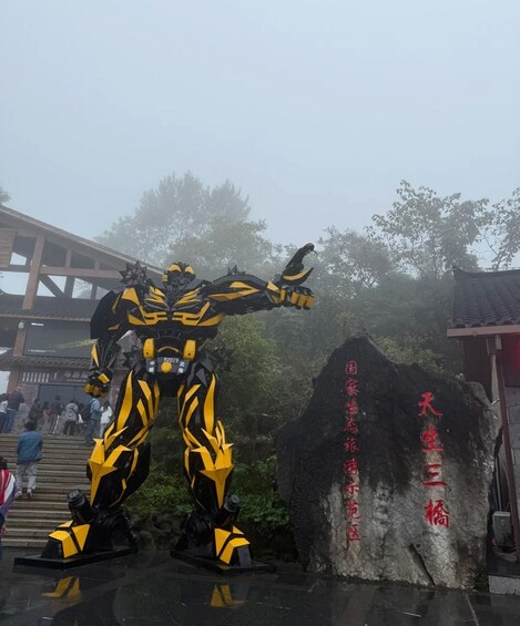 A large yellow and black statue of a character in a dynamic pose, a stone monument with red inscriptions, and a traditional building in the background. 5