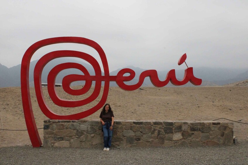 A person standing in front of a large red sign with the word 'Peru' on it, set against a mountainous backdrop. 2