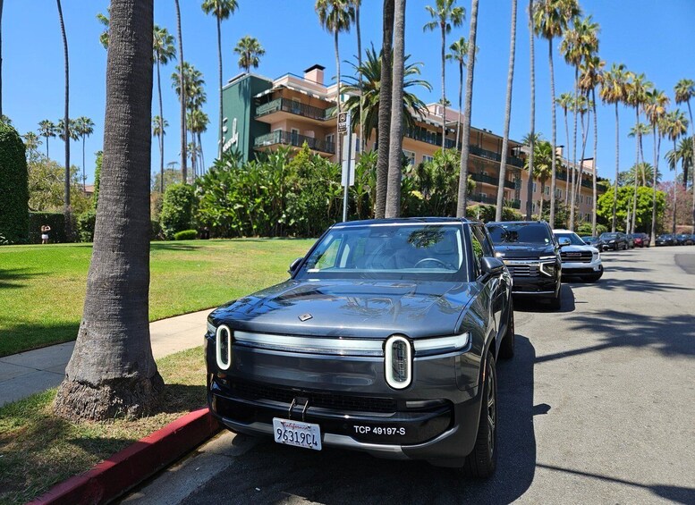 A black car parked on a street lined with palm trees and a building in the background. 4