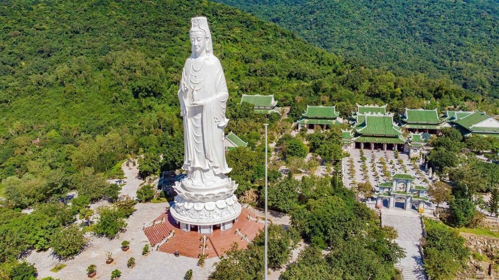 A large white statue in a natural setting with traditional architecture. 4