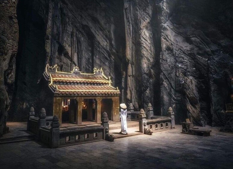 A traditional temple with a tiled roof, stone pillars, and a person in white robes standing in front. 1