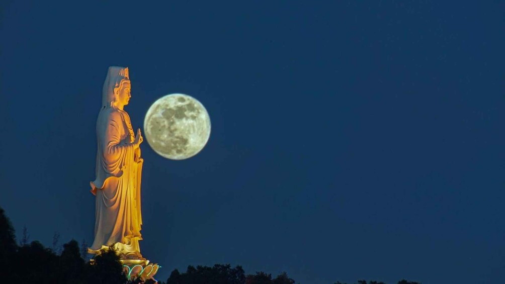 A statue of a robed figure with a full moon in the background. 3