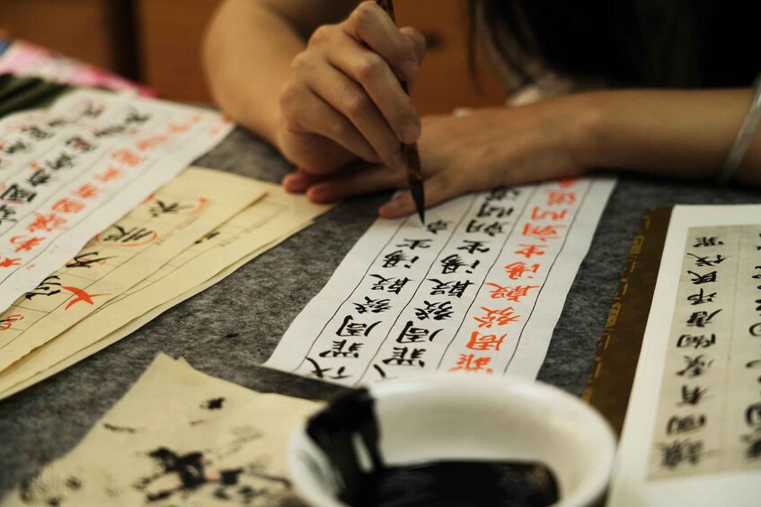 A person writing Chinese calligraphy on paper. 1